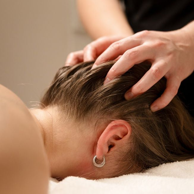 A close-up lifestyle shot of a person receiving a scalp massage, with hands massaging their hair while wearing a silver hoop earring.