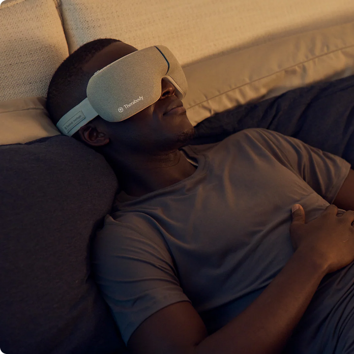 Person wearing a sleep mask lying on a couch in a dimly lit room