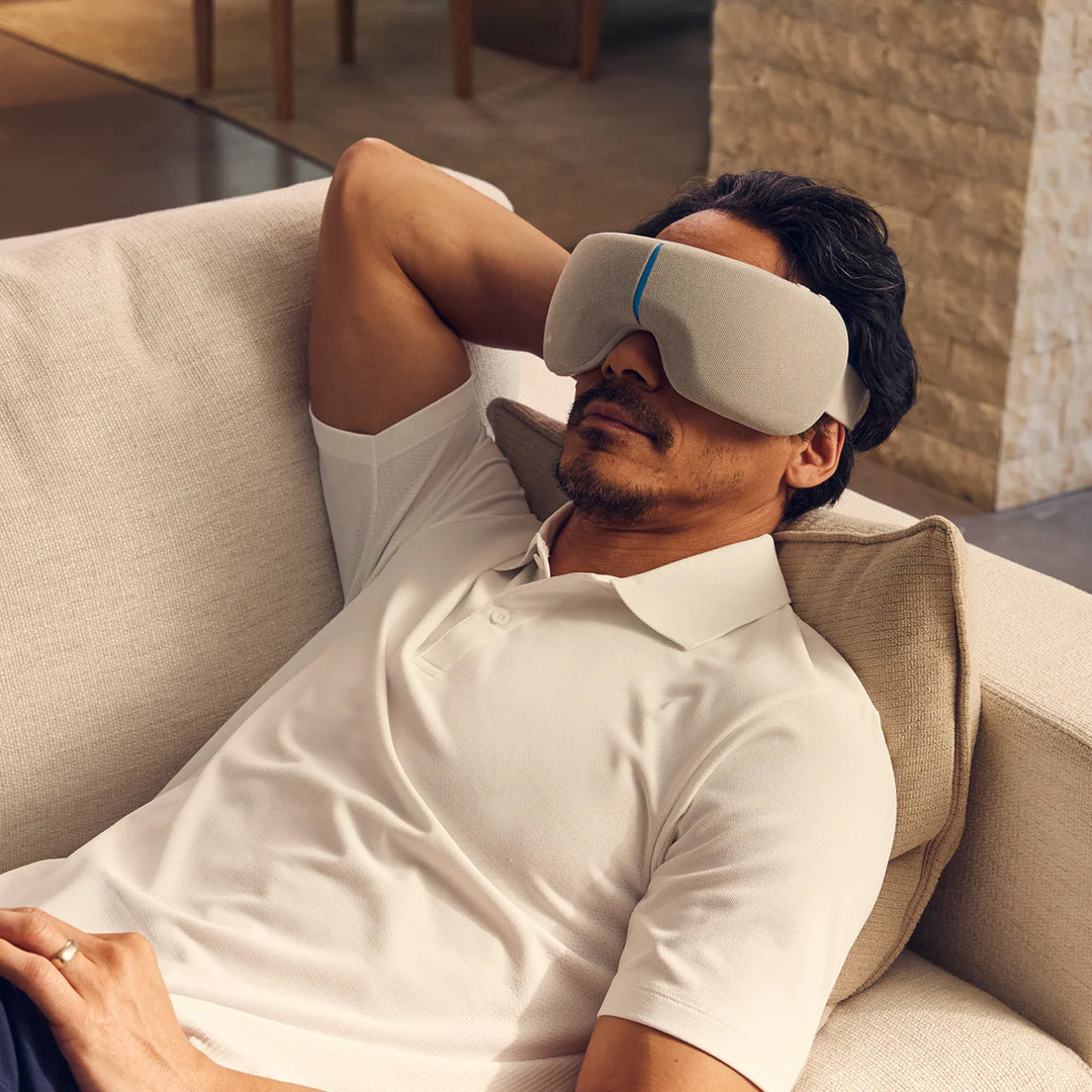 Man relaxing on a couch wearing a white sleep mask.