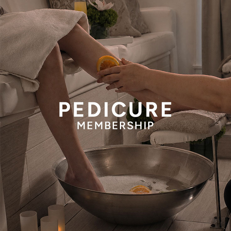A spa pedicure scene with a person's foot and lower leg resting in a metal bowl of bubbly bath water while another person applies an orange slice to the foot. Large overlaid text reads 'PEDICURE MEMBERSHIP'.
