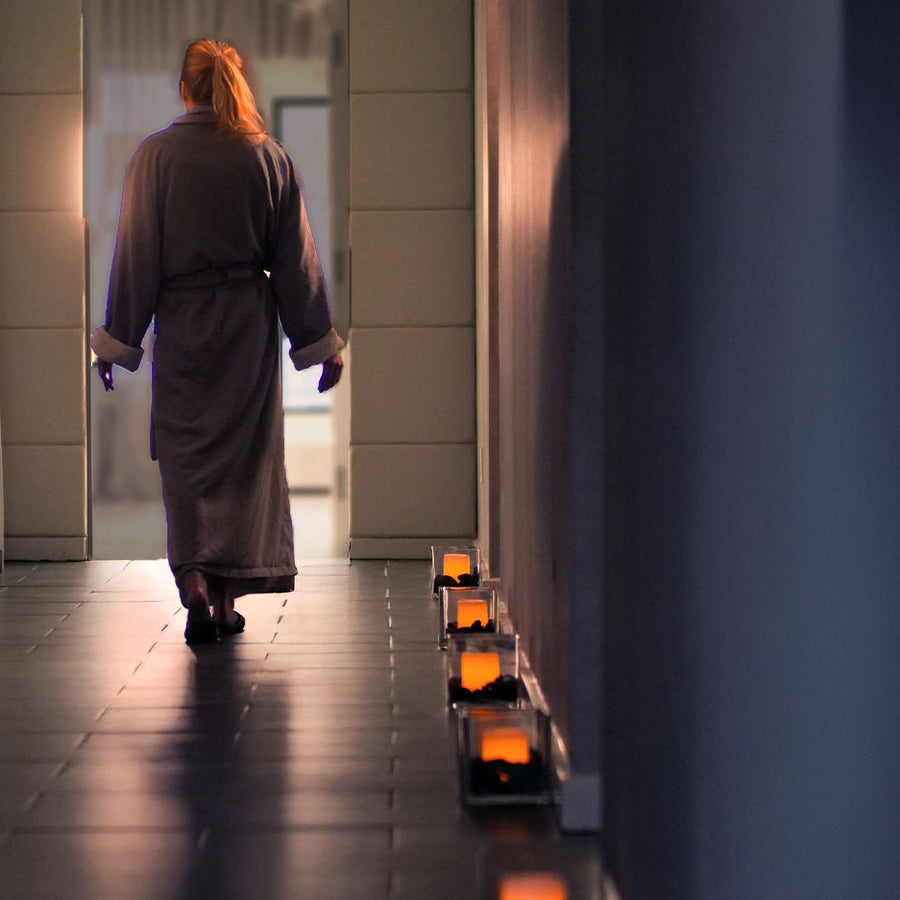 Person in a robe walking down a dimly lit hallway with candles lining the floor.
