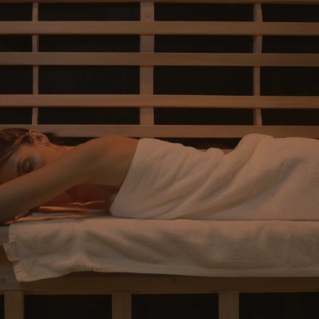 Person lying on a wooden bench in a dimly lit room, covered with a white towel.